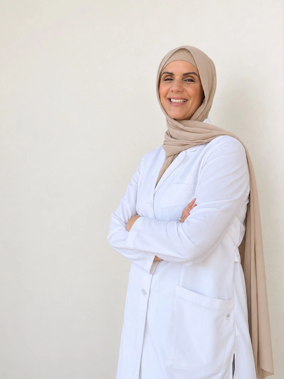 Esma El Merini smiling with her arms folded, in a white practitioner coat and a beige hijab