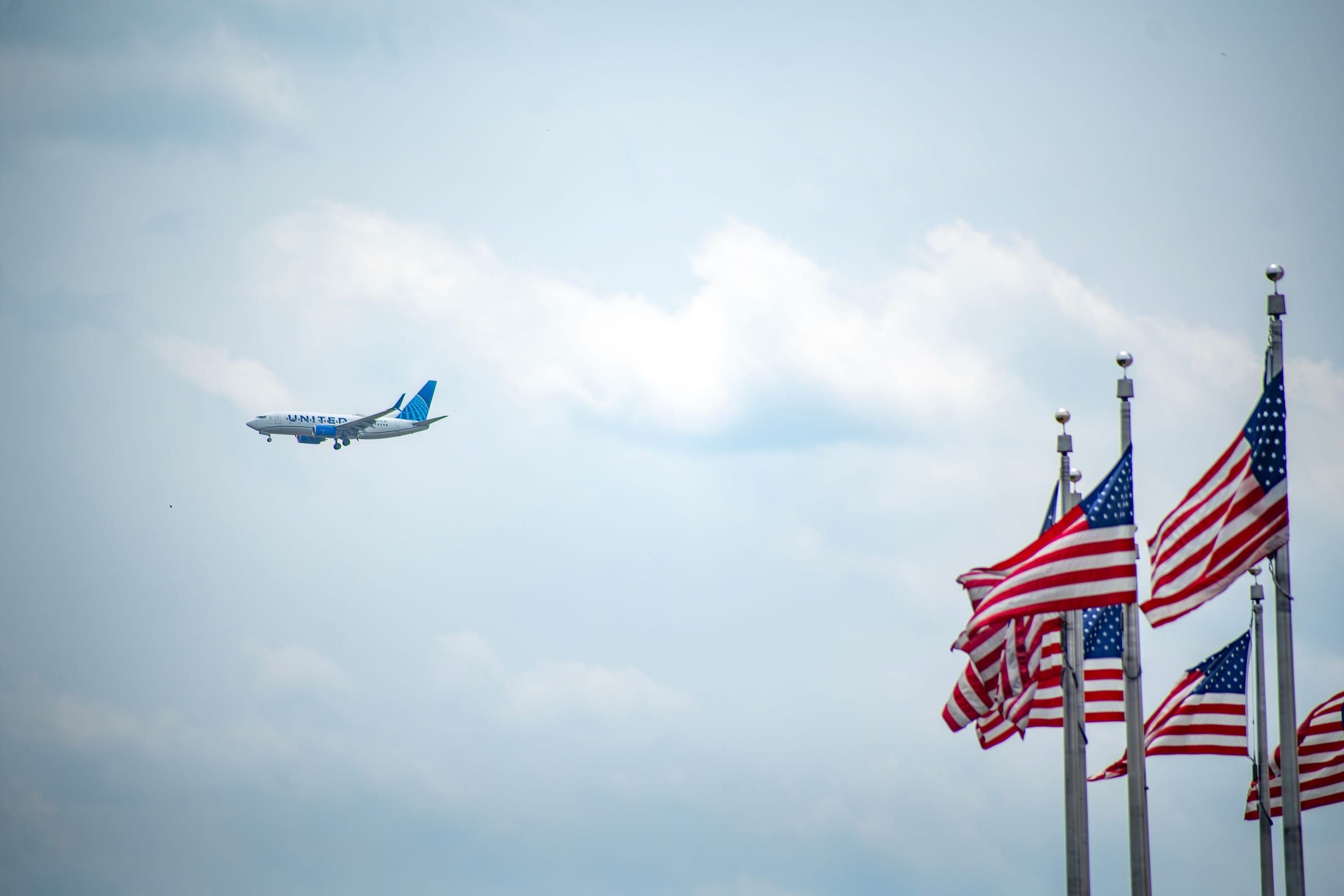 A passenger plane flying past American flags under a pale blue sky