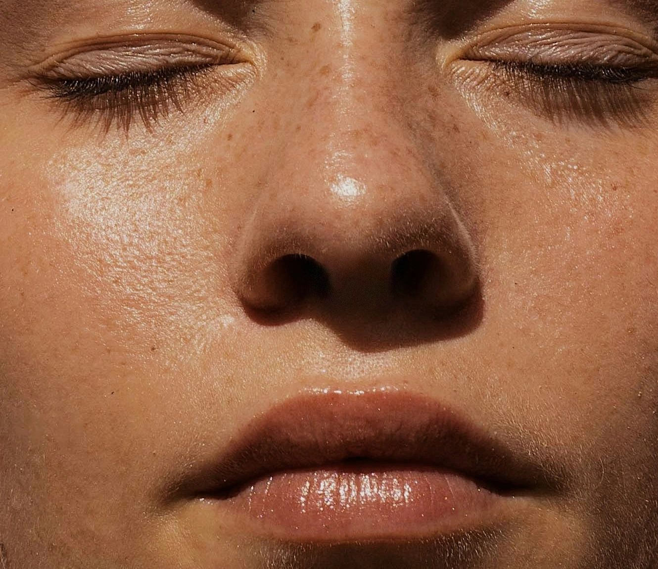 Close-up of a woman's face with her eyes closed, freckled skin glowing in warm light