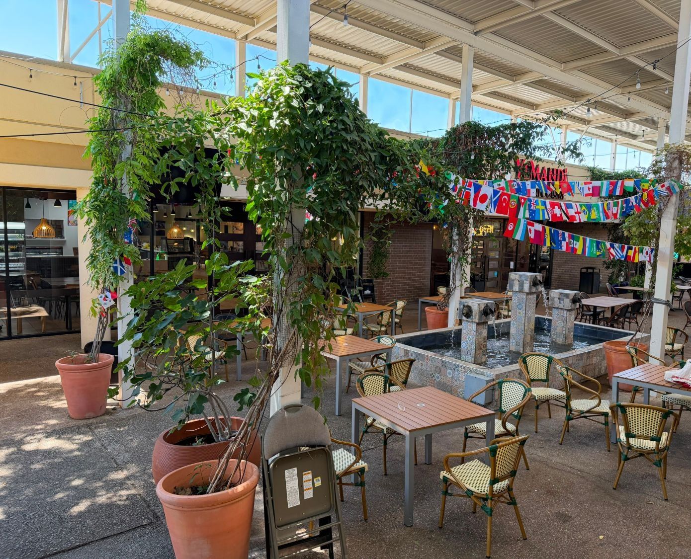 A covered courtyard with a tiled fountain, café tables, potted plants and string lights