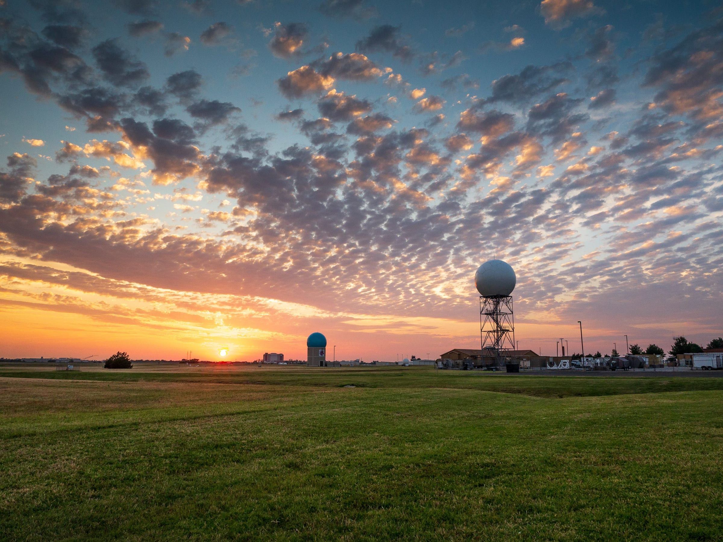 Sunset over a grass field in Norman, Oklahoma, with weather radar domes on the horizon