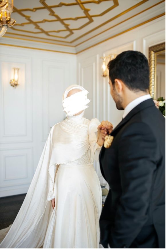 A bride in a white gown and veil and a groom in a dark suit, holding hands in a room with gold detailing