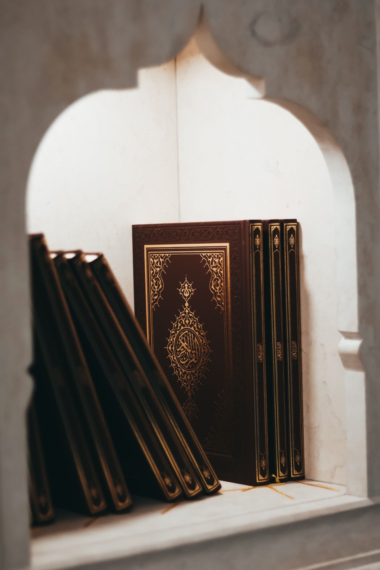 Copies of the Quran bound in brown leather and gold, resting on a shelf inside a white arched niche